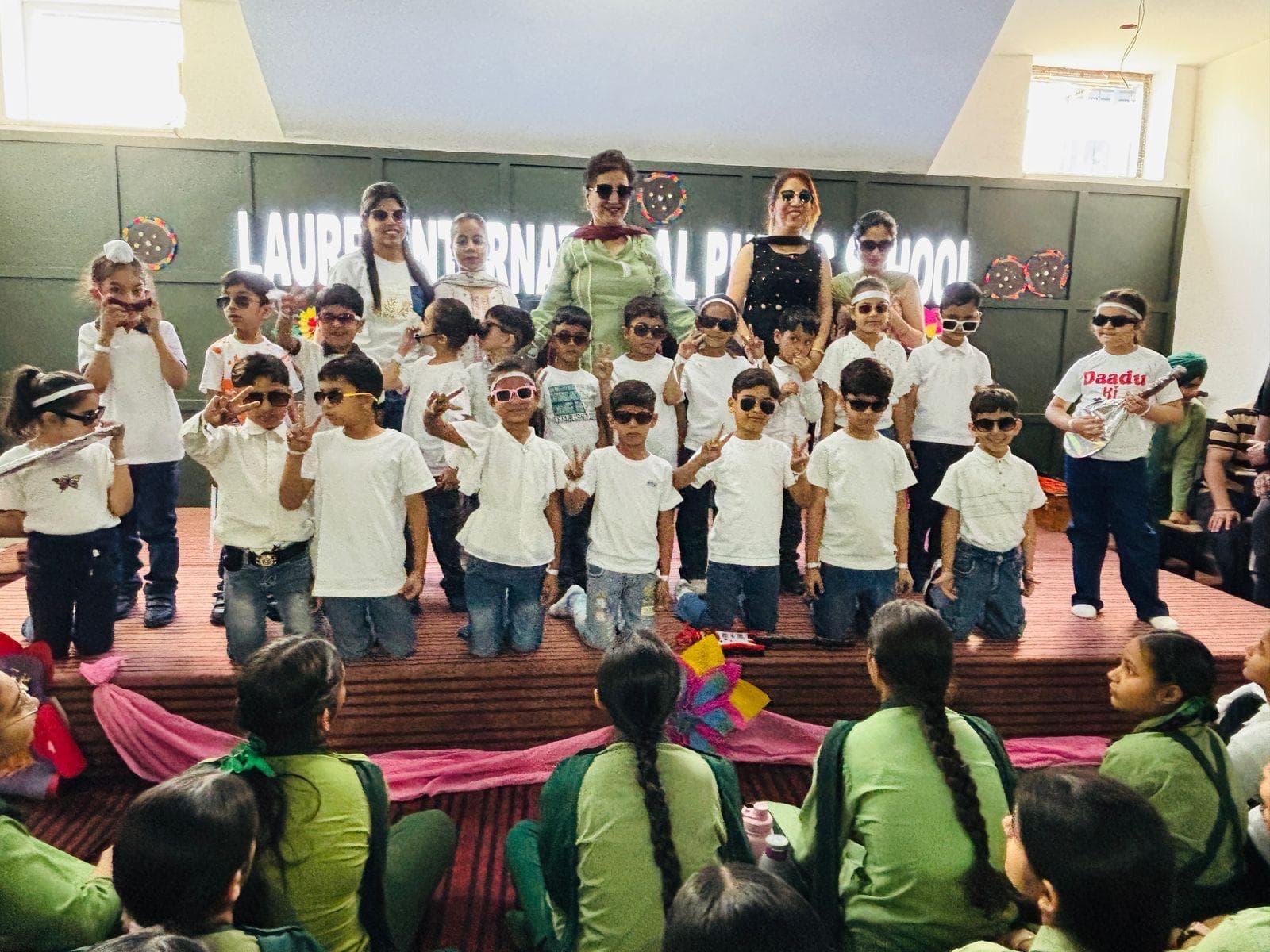 Students in white T-shirts and sunglasses performing on stage